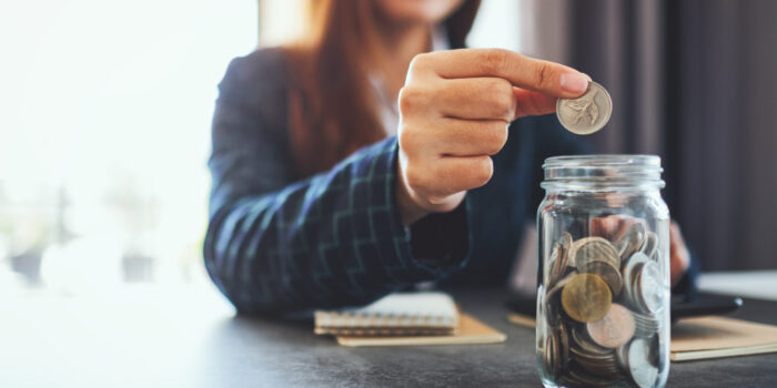 Closeup image of a businesswoman collecting and putting coins in a glass jar