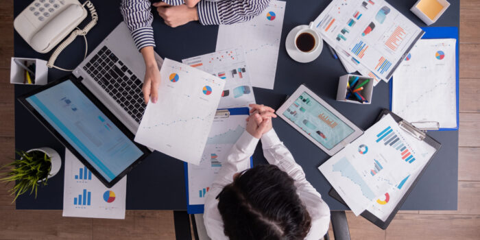 Top view of office workers meeting analyzing financial charts holding clipboard. Manager and employer discussing marketing strategy during briefing. Pointing at graphs.